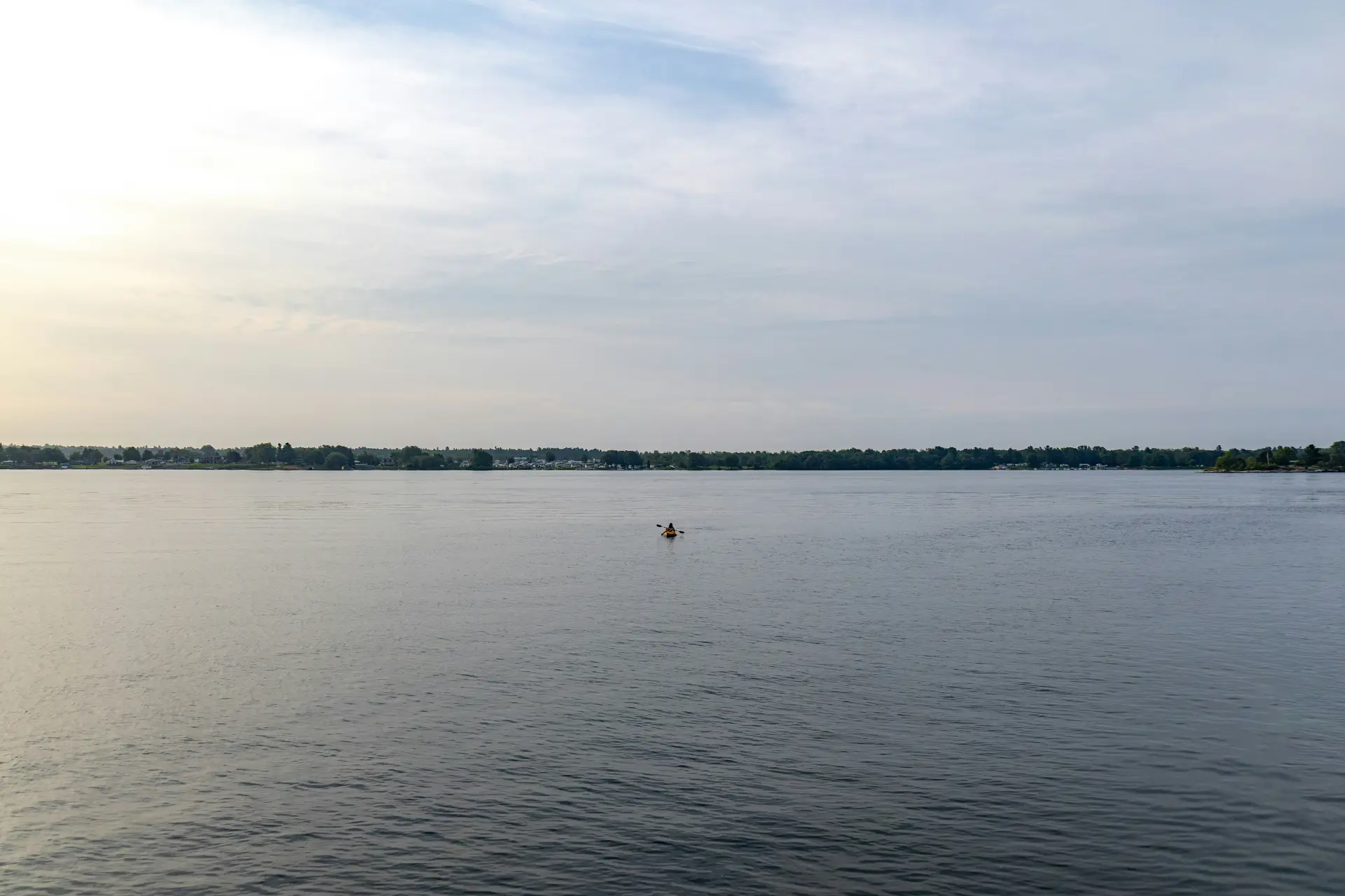 Large fleuve calme sous la lumière du matin, un kayak seul au loin